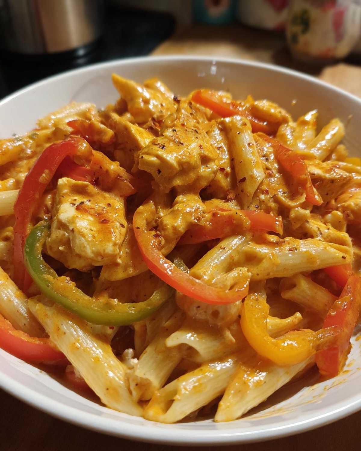 Close-up of a white bowl filled with creamy rasta pasta, chicken pieces, and colorful bell pepper strips.
