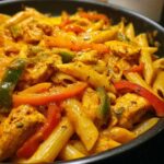 Close-up of creamy, orange-sauced rasta pasta mixed with chunks of chicken and sliced red and green bell peppers.