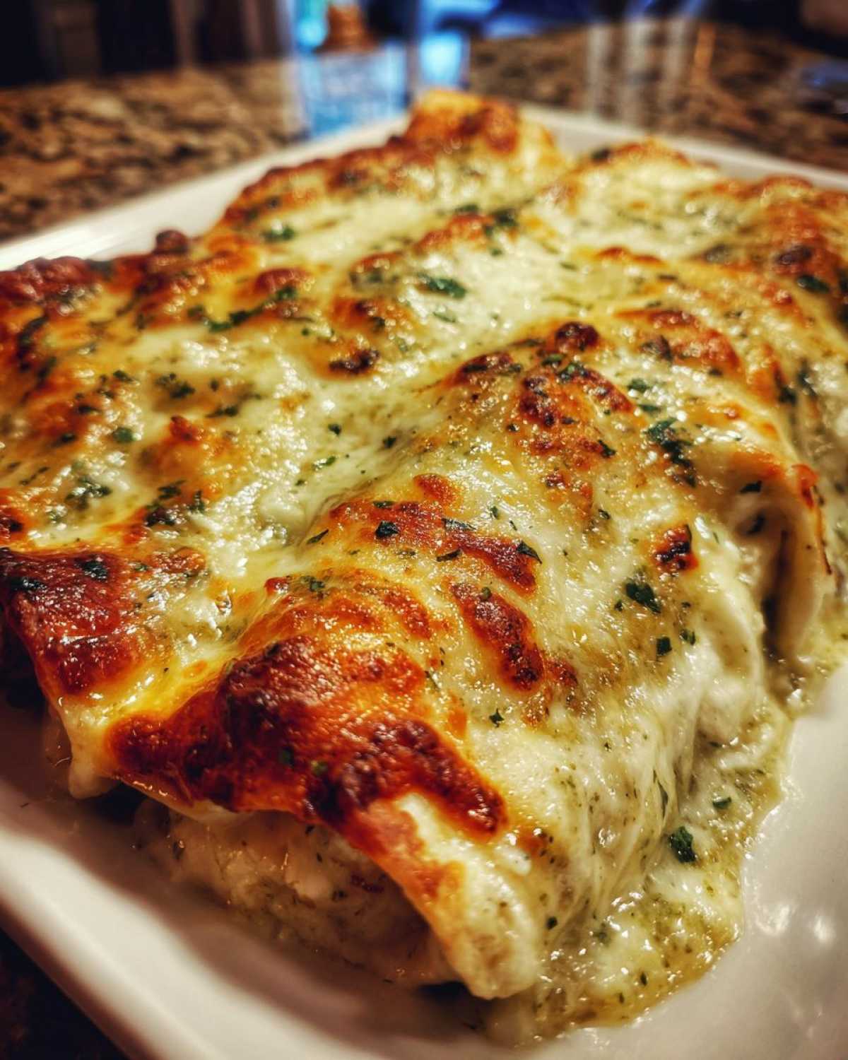Close-up of baked Creamy White Chicken Enchiladas with green chile sauce and melted, browned cheese topping.