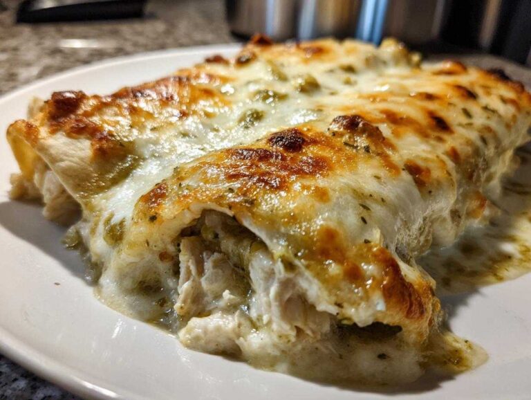 Close-up of baked Creamy White Chicken Enchiladas covered in melted, browned cheese and green chile sauce.