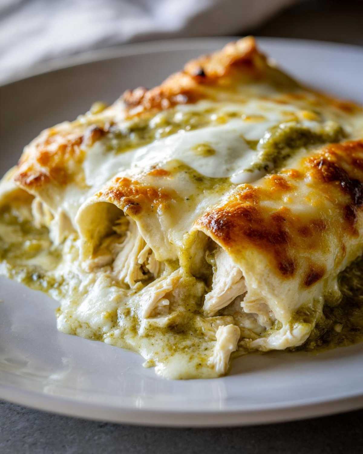 Close-up of Creamy White Chicken Enchiladas, showing shredded chicken and melted, browned cheese.