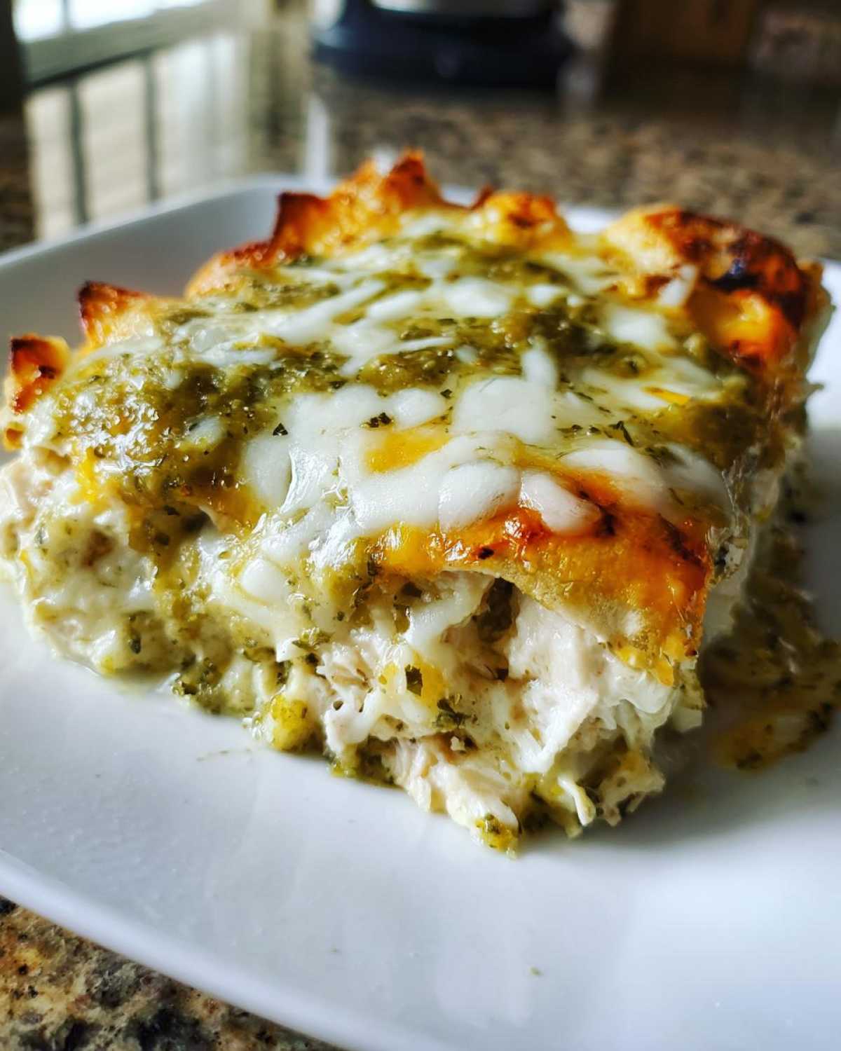 Close-up of a serving of Creamy White Chicken Enchiladas topped with melted white cheese and green chile sauce.
