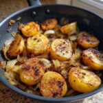 Close-up of perfectly crispy fried potatoes halves mixed with browned onions in a black skillet.