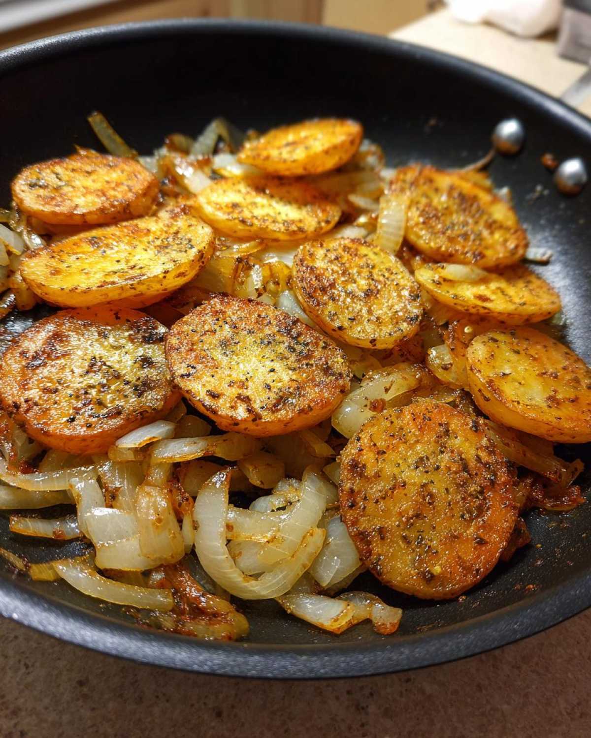 Close-up of golden brown, seasoned fried potatoes and caramelized onions cooking in a black skillet.
