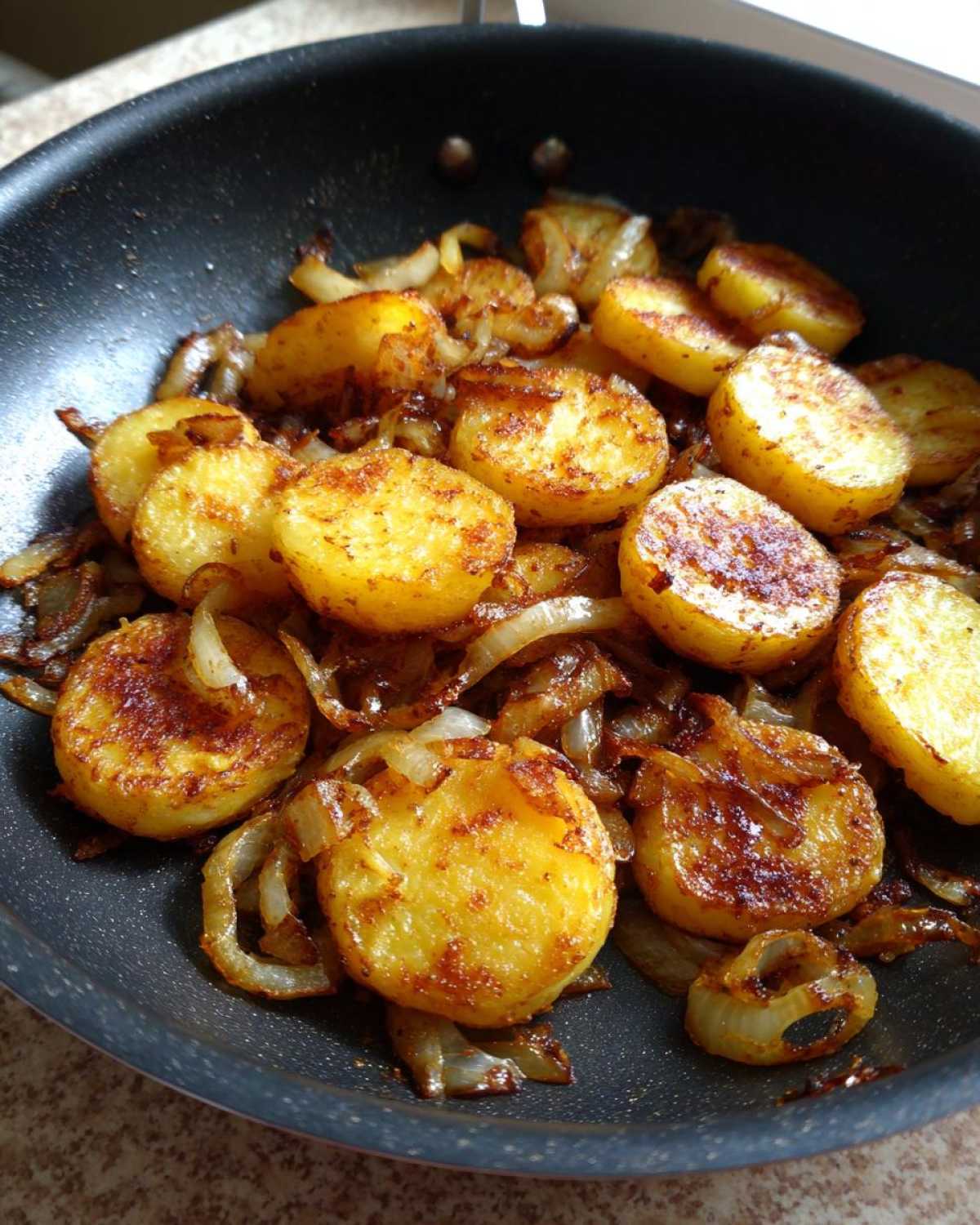 Close-up of perfectly golden and crispy fried potatoes mixed with caramelized onions in a black skillet.