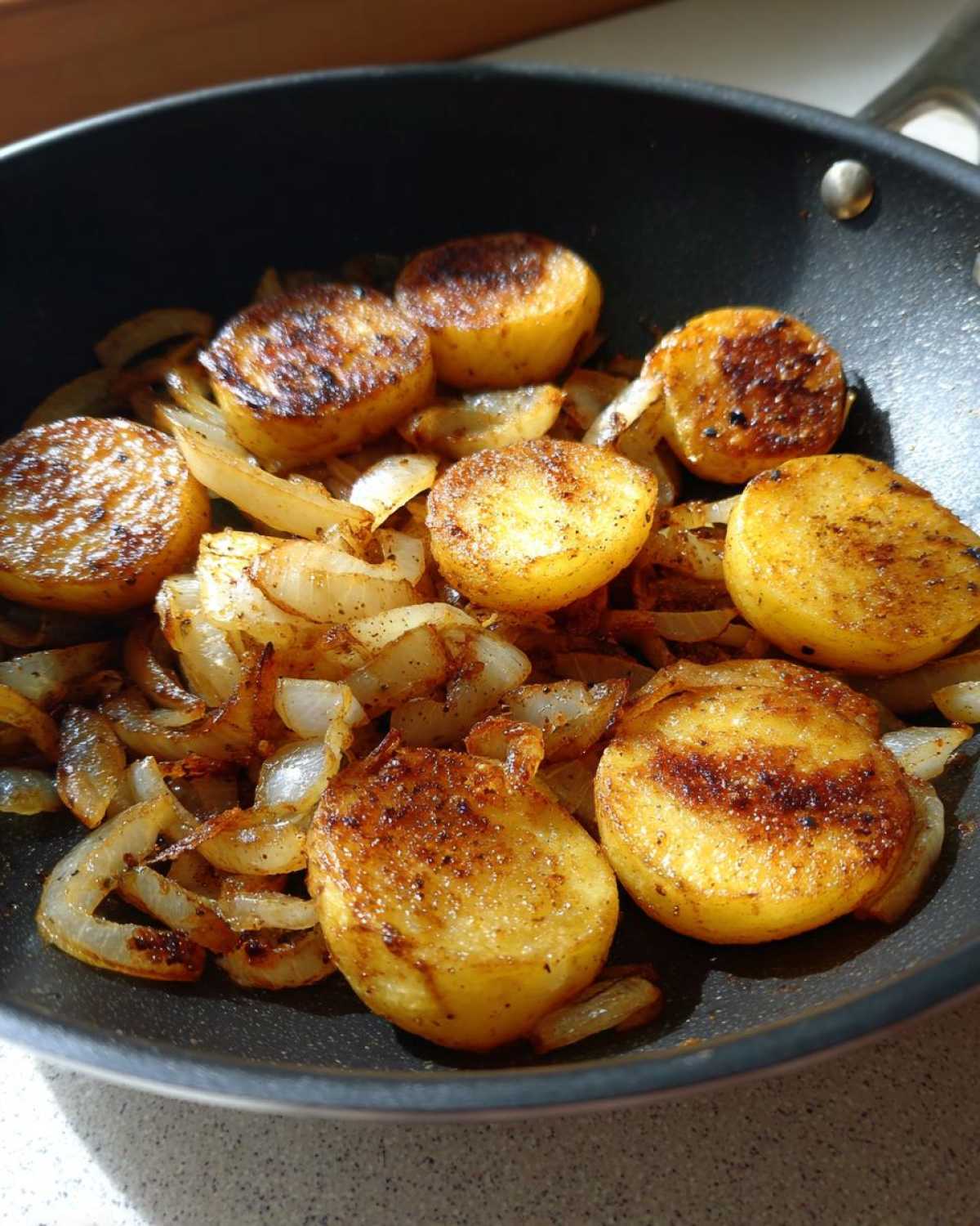 Close-up of golden brown, perfectly seared fried potatoes and caramelized onions cooking in a black skillet.
