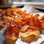Close-up of golden brown, crispy oven Parmesan potato chips scattered on parchment paper.