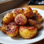 Close-up of golden brown, crispy roast potatoes seasoned with herbs on a white plate.
