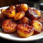 A close-up of golden brown, incredibly crispy roast potatoes piled high on a white serving dish.