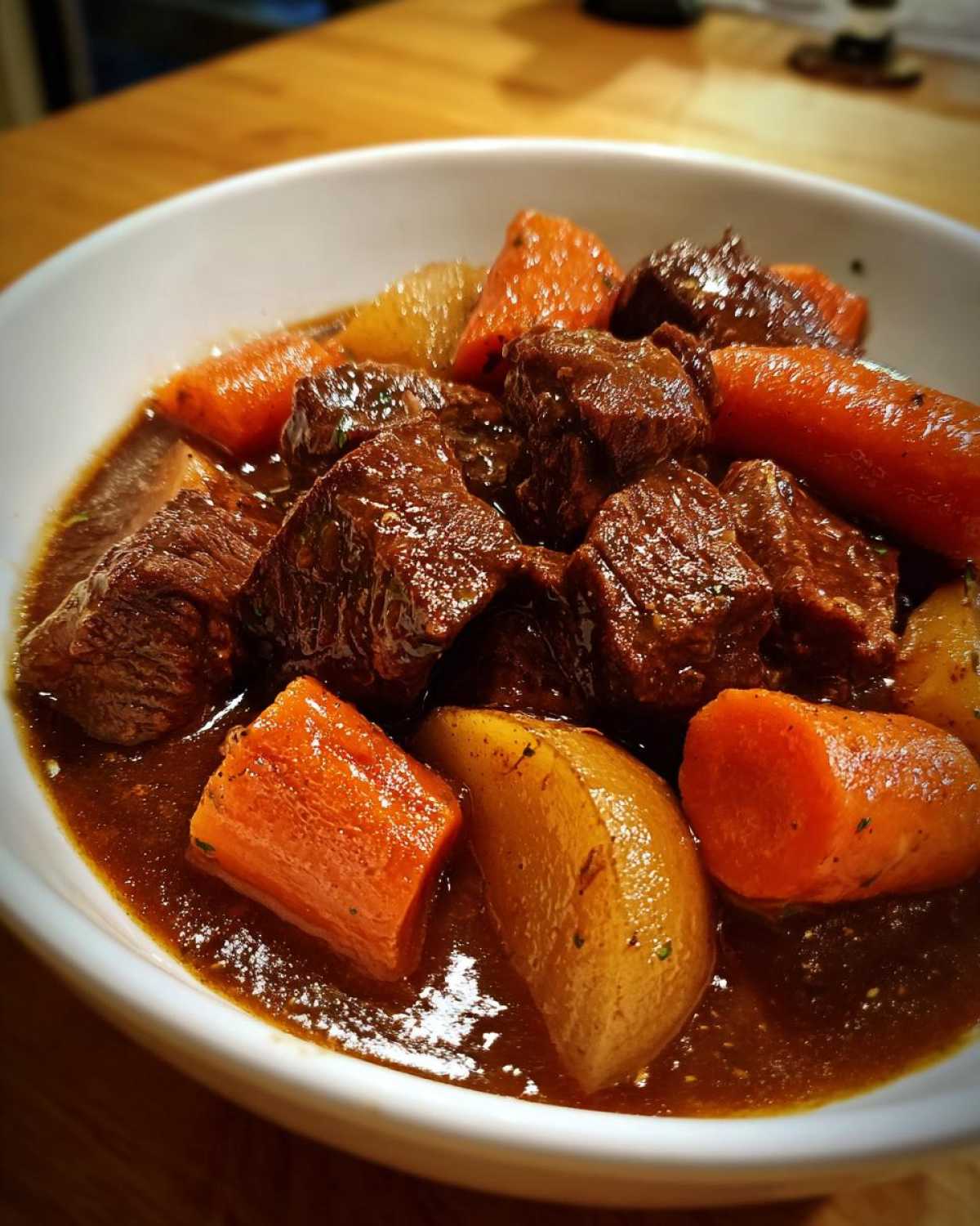 Close-up of a white bowl filled with Easy Guinness Beef Stew featuring chunks of beef, carrots, and potatoes in a rich, dark sauce.