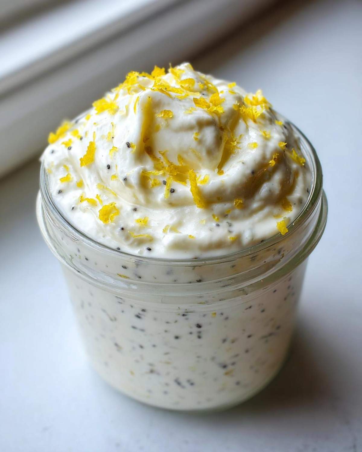 Close-up of an Easy Lemon Poppy Seed Yogurt Parfait topped with bright yellow lemon zest in a glass jar.