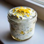 Close-up of an Easy Lemon Poppy Seed Yogurt Parfait topped with bright yellow lemon zest in a glass jar.
