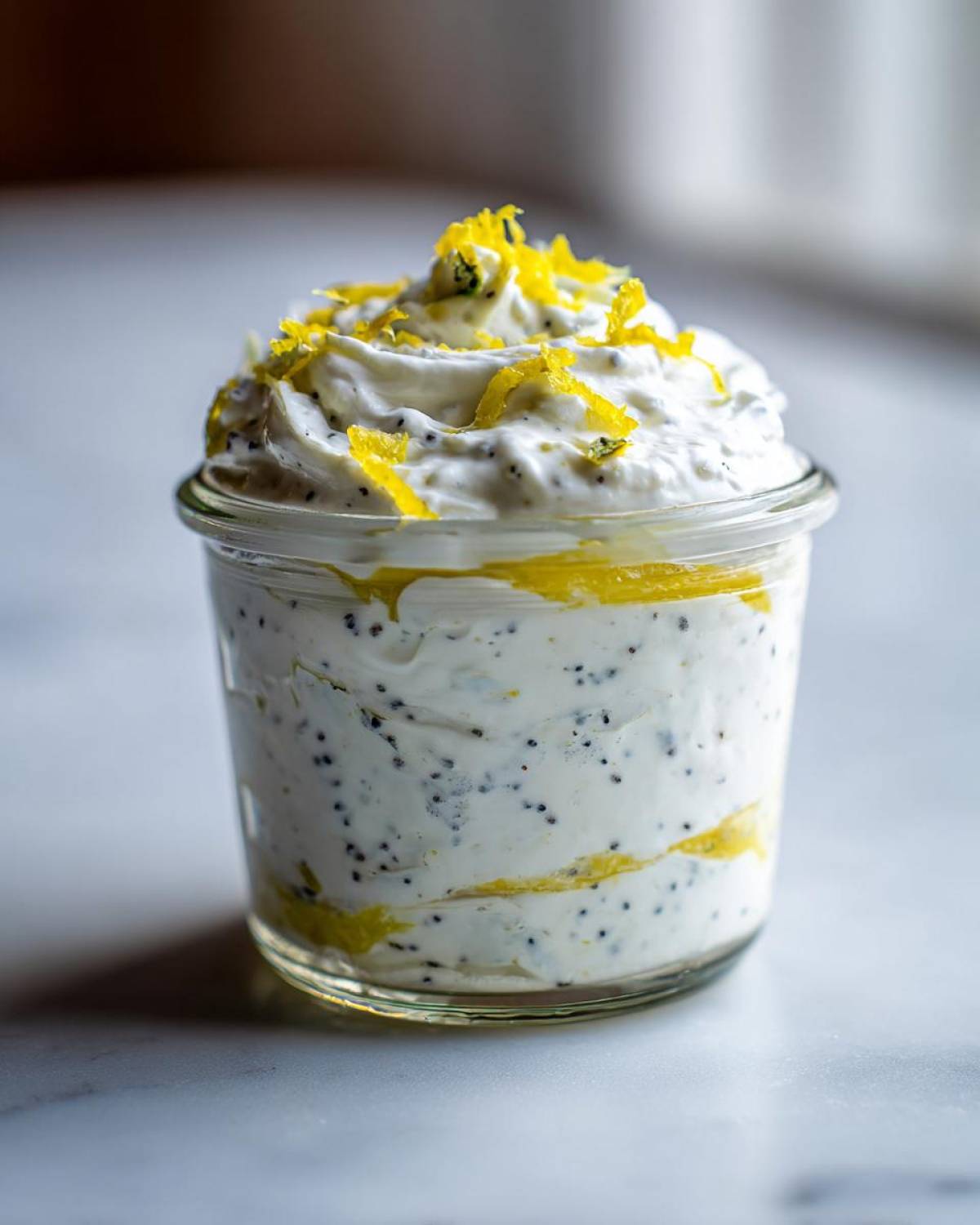 Close-up of an Easy Lemon Poppy Seed Yogurt Parfait layered with lemon curd and topped with bright yellow lemon zest.