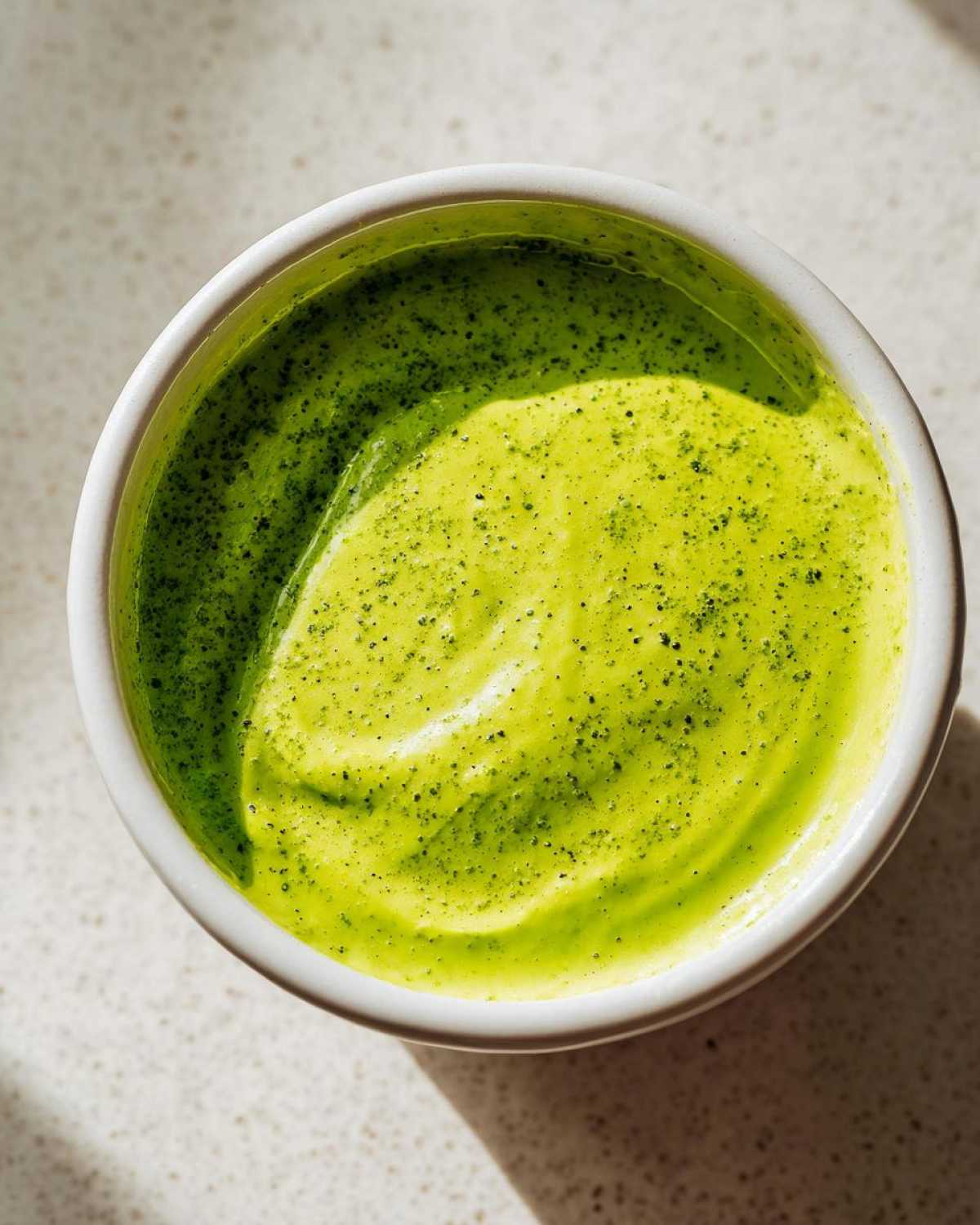 Overhead view of bright green Five-Minute Avocado Lime Dressing swirled in a small white bowl.
