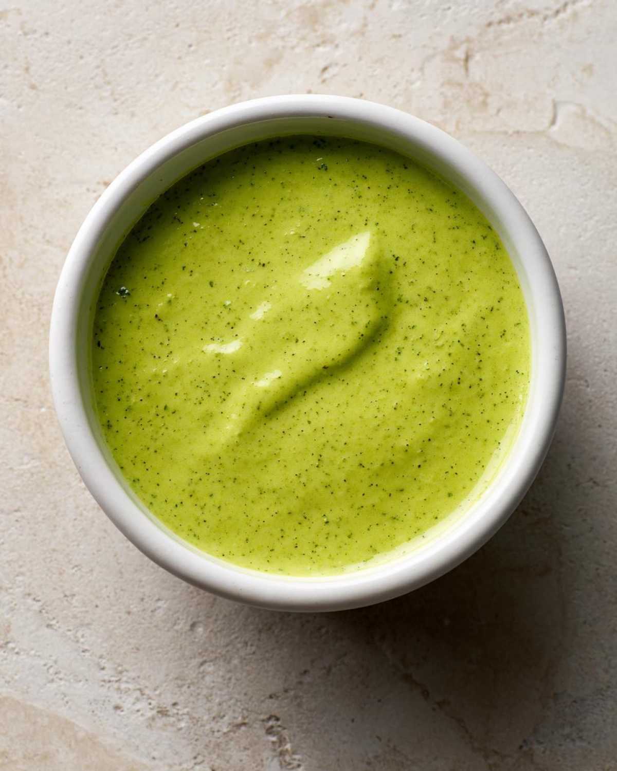 Overhead shot of creamy, bright green Five-Minute Avocado Lime Dressing in a small white bowl.