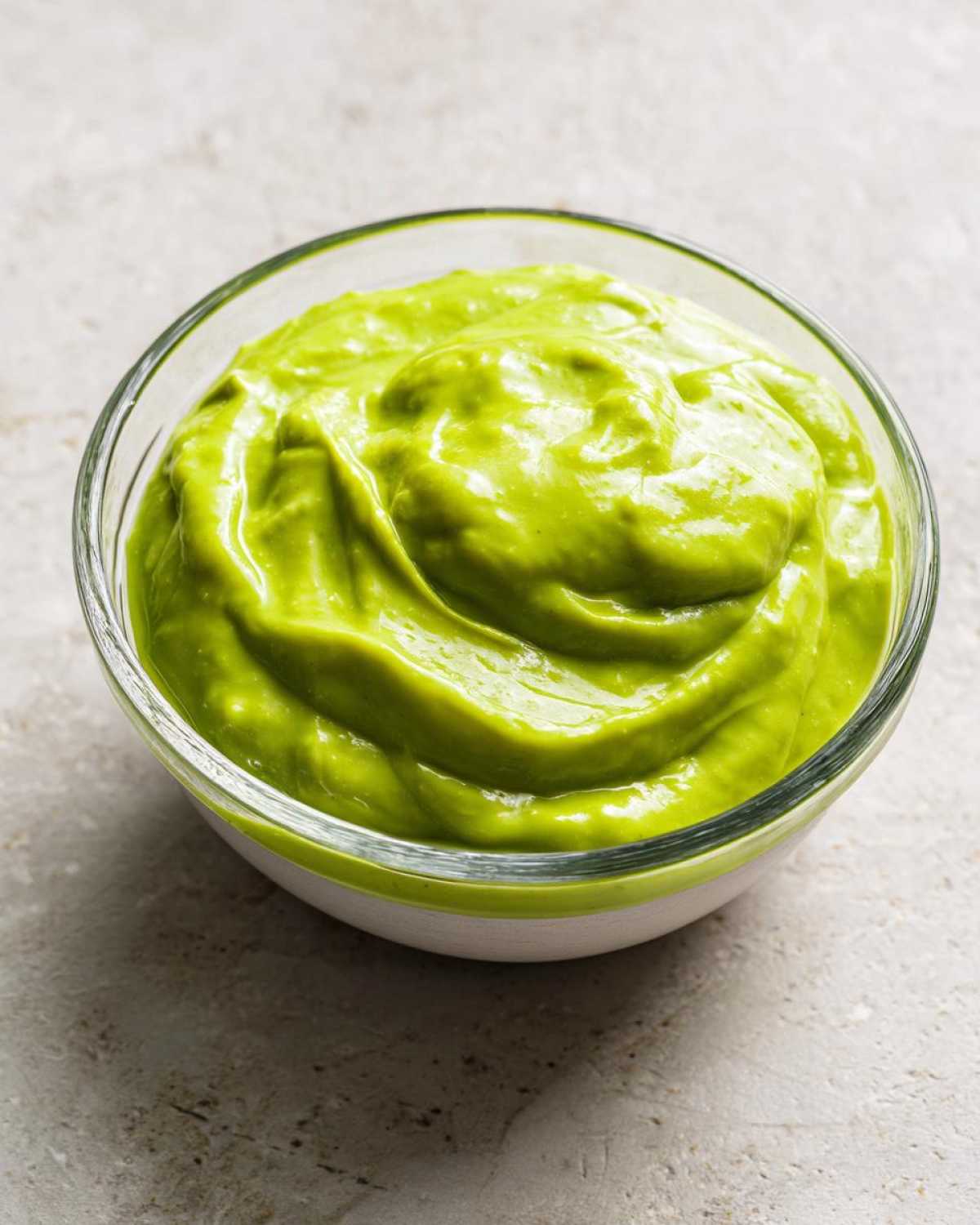 Close-up of thick, bright green Five-Minute Avocado Lime Dressing swirled in a small glass bowl.