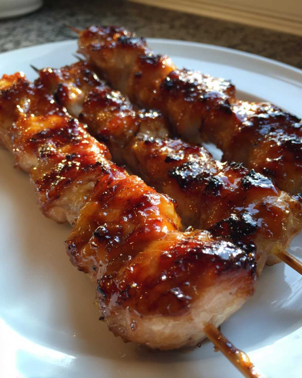Close-up of three perfectly grilled, glazed chicken skewers with caramelized edges.