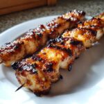 Close-up of perfectly grilled and glazed chicken skewers resting on a white plate.
