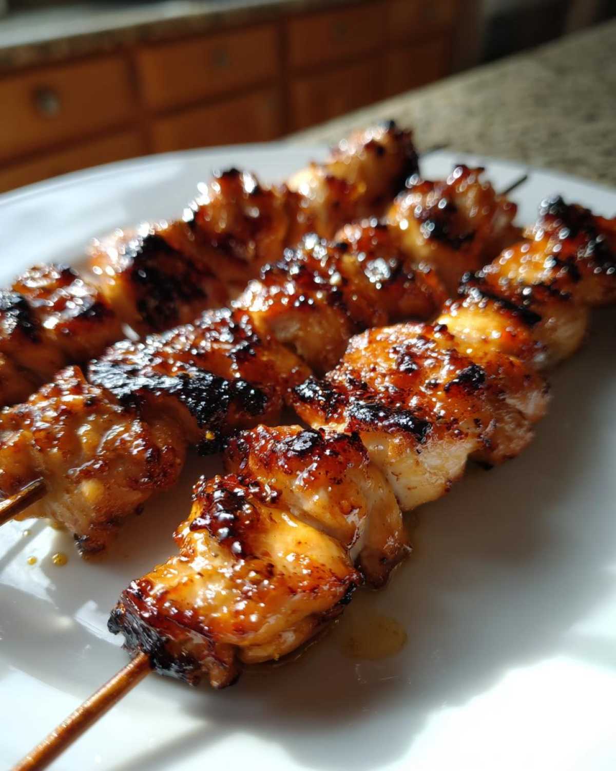 Close-up of three juicy, glazed chicken skewers with caramelized edges resting on a white plate.