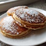 A stack of fluffy High-Protein Cottage Cheese Pancakes dusted generously with powdered sugar on a white plate.