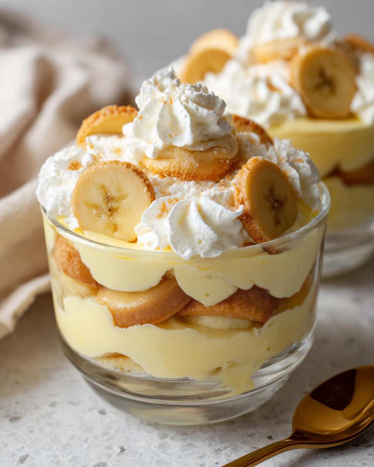 Close-up of individual banana pudding layered with vanilla wafers, custard, bananas, and topped with whipped cream.