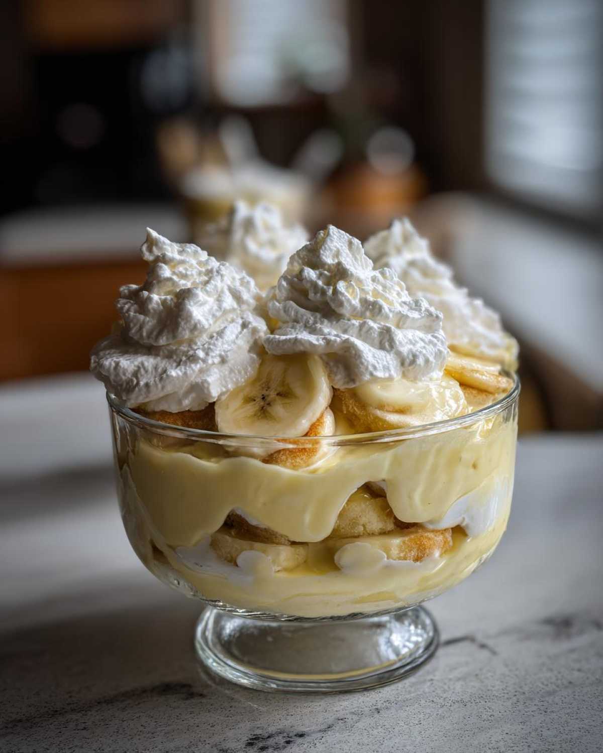 Close-up of an individual serving of creamy banana pudding layered with vanilla wafers and topped with whipped cream and banana slices.