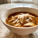 Close-up of a white bowl filled with rich broth, shredded chicken, and rice noodles for Instant Pot Chicken Pho.