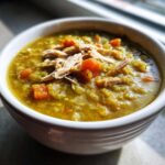 Close-up of a white bowl filled with thick, green Instant Pot Split Pea Soup with smoked turkey and diced carrots.