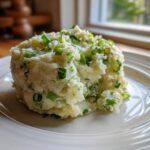 A mound of creamy Irish Champ mashed potatoes with visible chunks and topped generously with chopped green scallions.