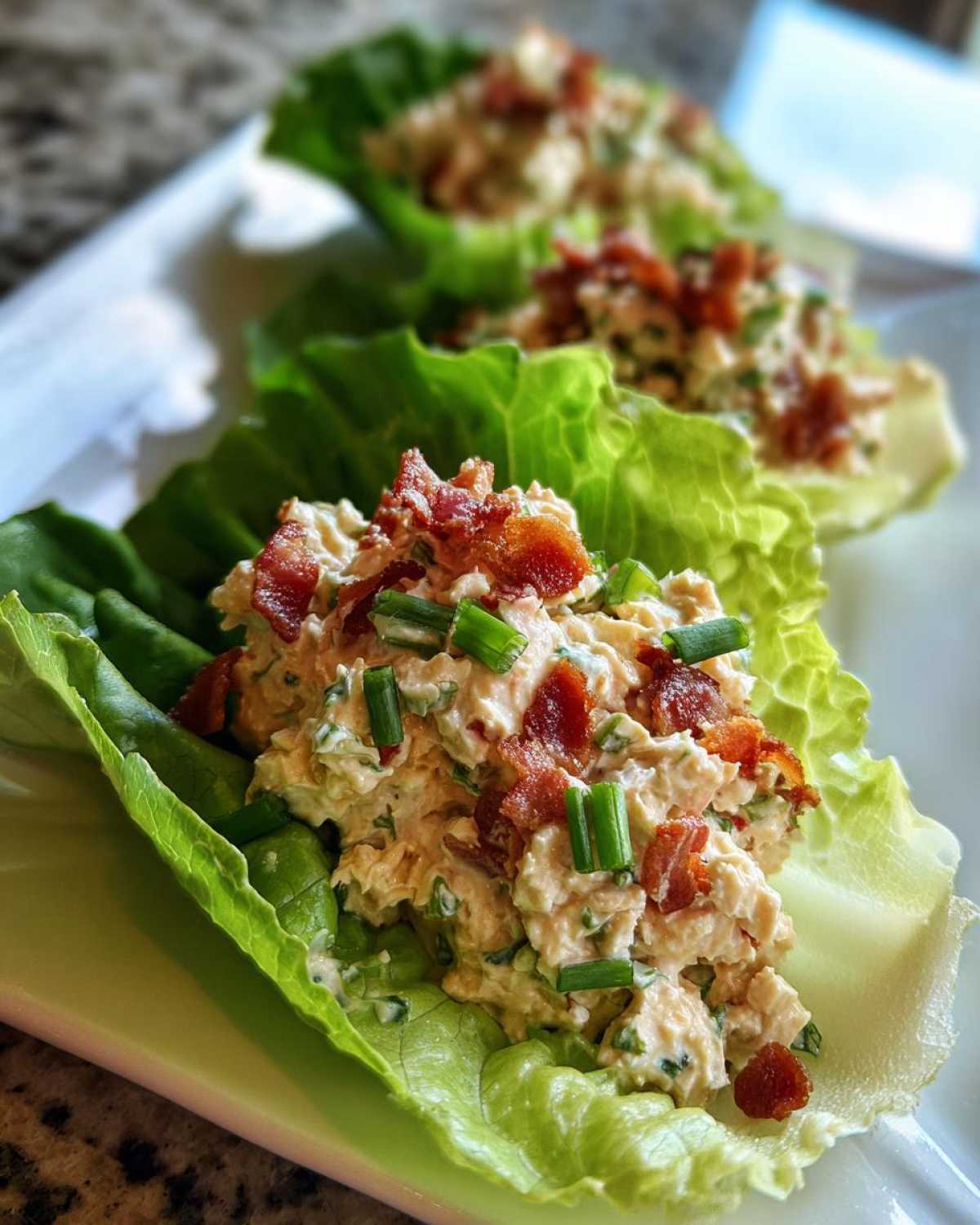 Close-up of Keto Bacon Ranch Chicken Salad served in crisp lettuce cups, topped with bacon bits and chives.