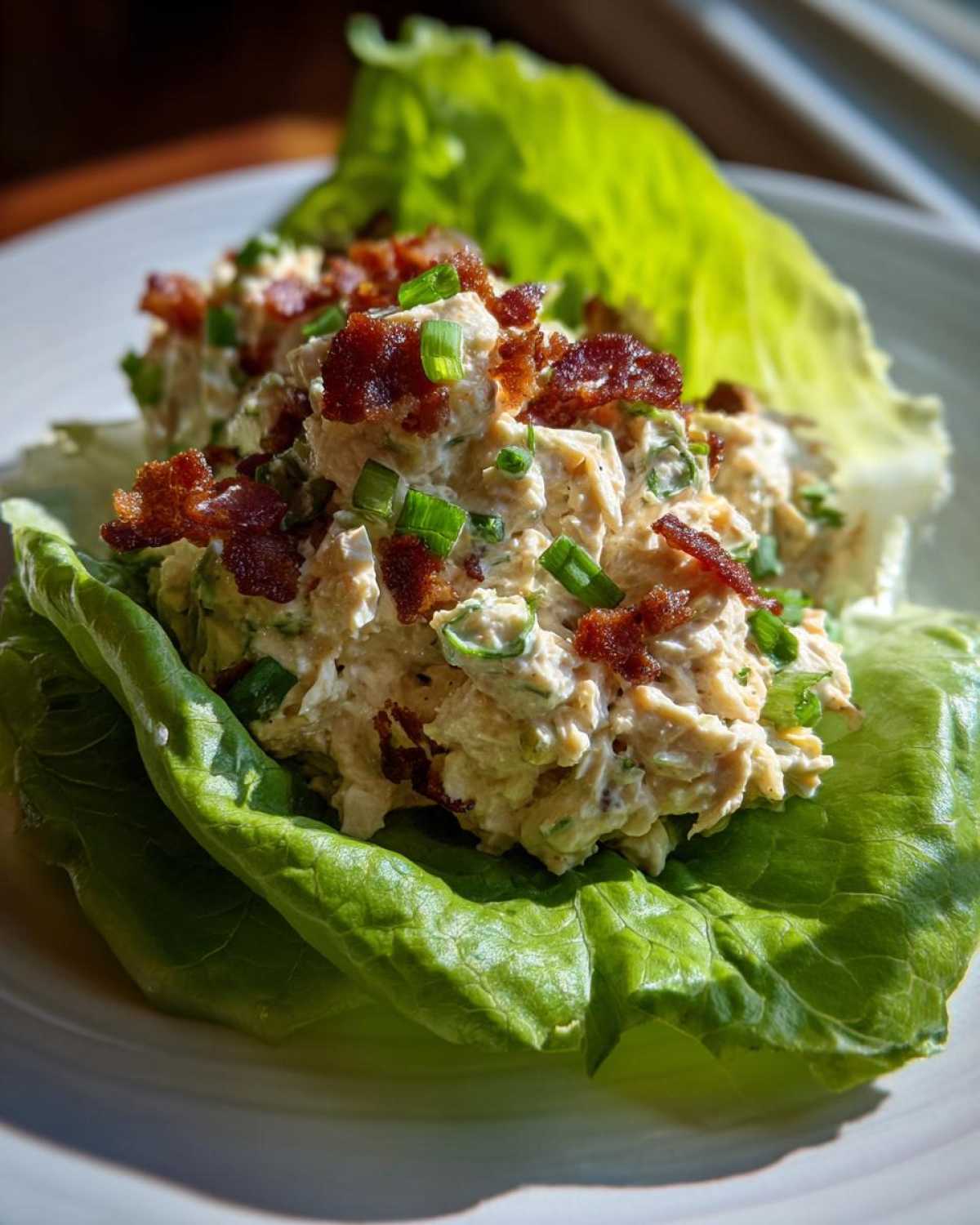 Close-up of Keto Bacon Ranch Chicken Salad served in crisp lettuce cups, topped with bacon bits and chives.