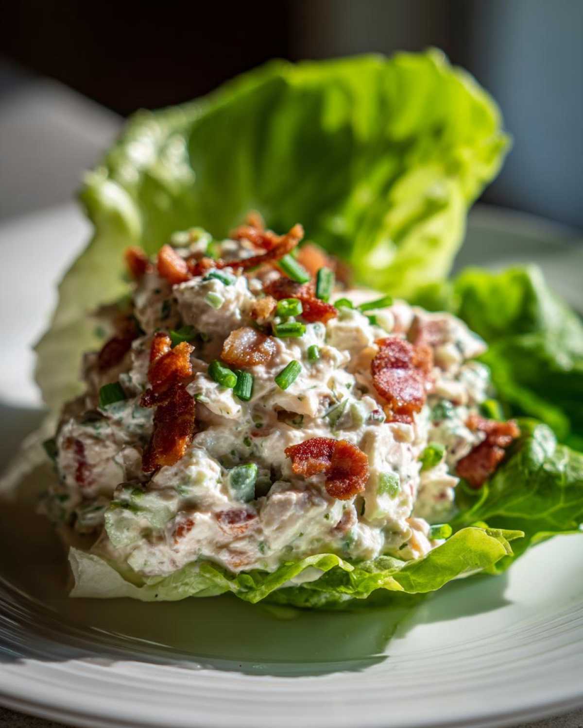 A serving of Keto Bacon Ranch Chicken Salad nestled inside crisp lettuce leaves, topped with bacon bits and chives.