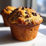 Close-up of a perfectly baked, moist banana chocolate chip muffin topped with melted chocolate chips.