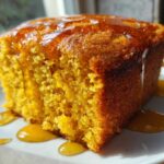 Close-up of a moist slice of bright orange sweet potato cornbread drizzled generously with honey on a white plate.