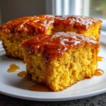A close-up of a moist slice of sweet potato cornbread generously drizzled with a shiny amber glaze on a white plate.