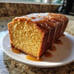 A slice of moist sweet potato pound cake generously drizzled with caramel sauce, sitting on a white plate.