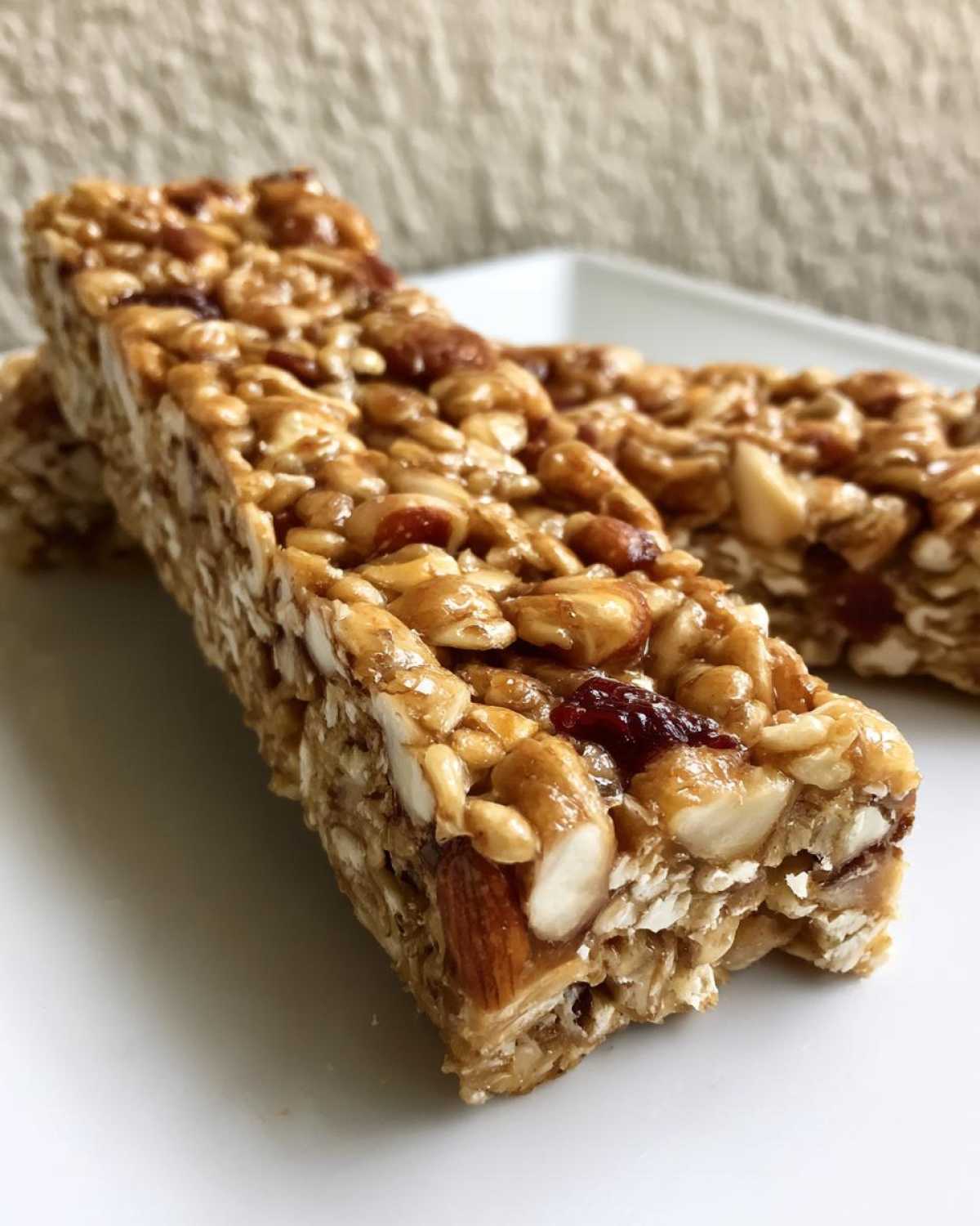 Close-up of two chewy no bake granola bars packed with oats, almonds, and sunflower seeds on a white plate.