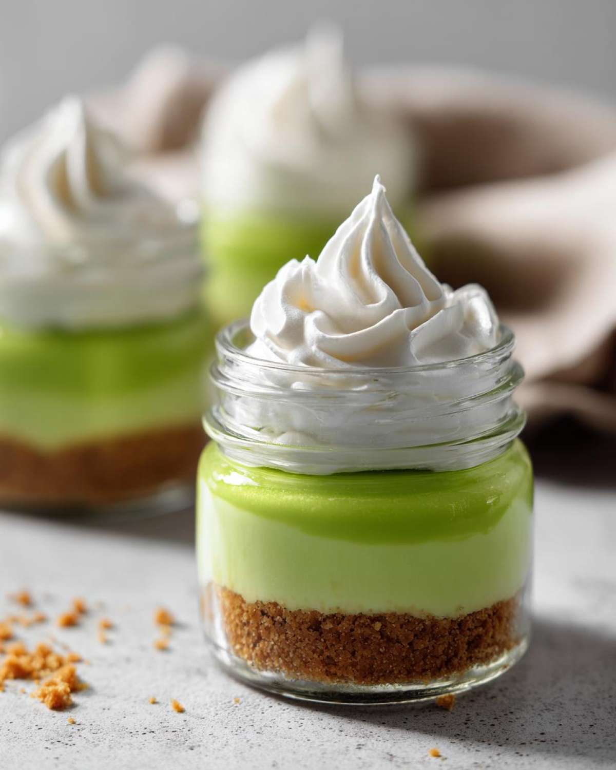 Close-up of a No-Bake Key Lime Pie Jar featuring a graham cracker crust, bright green filling, and a swirl of whipped cream.