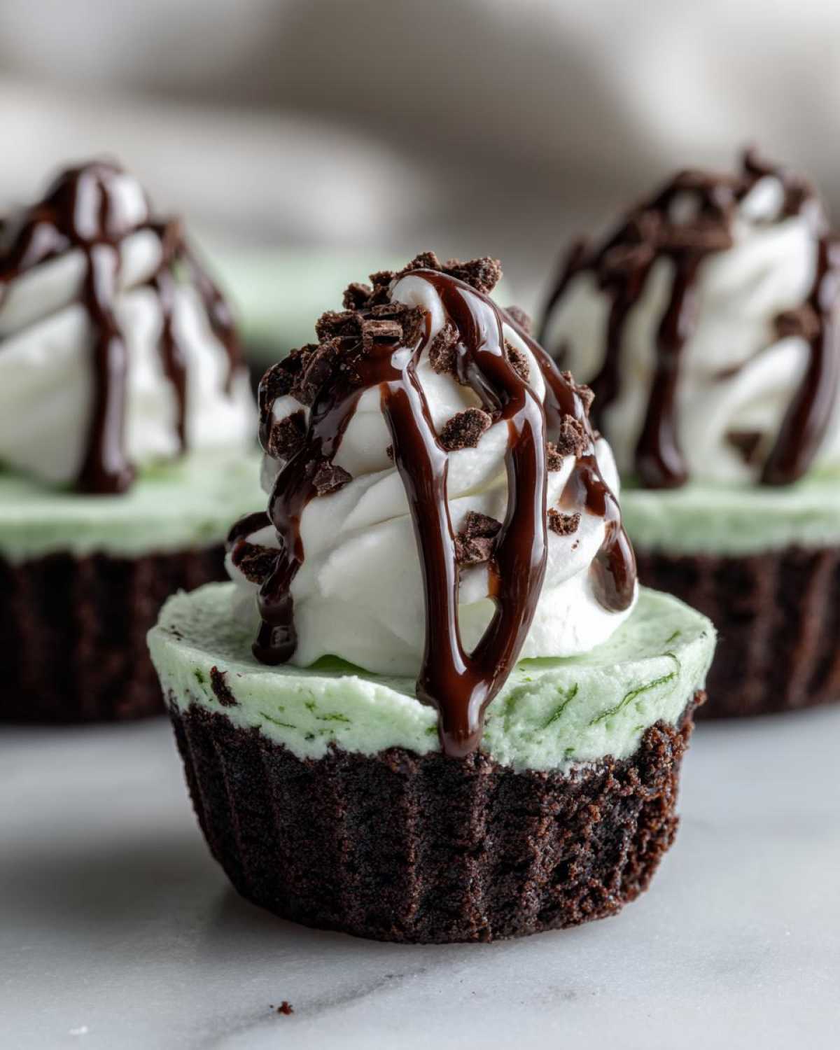 A close-up of a No-Bake Mint Chocolate Cheesecake Cup with a chocolate crust, mint filling, whipped topping, chocolate drizzle, and crumbs.