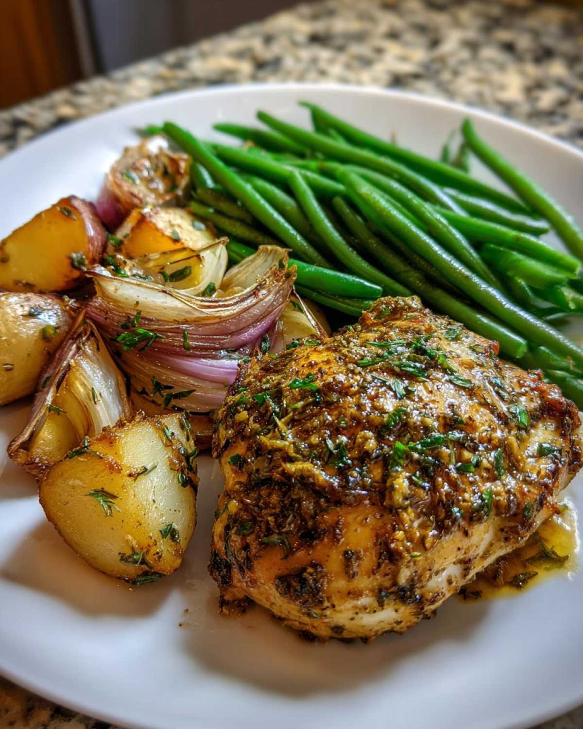 A serving of One-Pan Dijon Chicken with green beans, roasted potatoes, and red onions on a white plate.