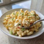 A spoonful of creamy Copycat Deli-Style Macaroni Salad, showing elbow macaroni, celery, and egg pieces.