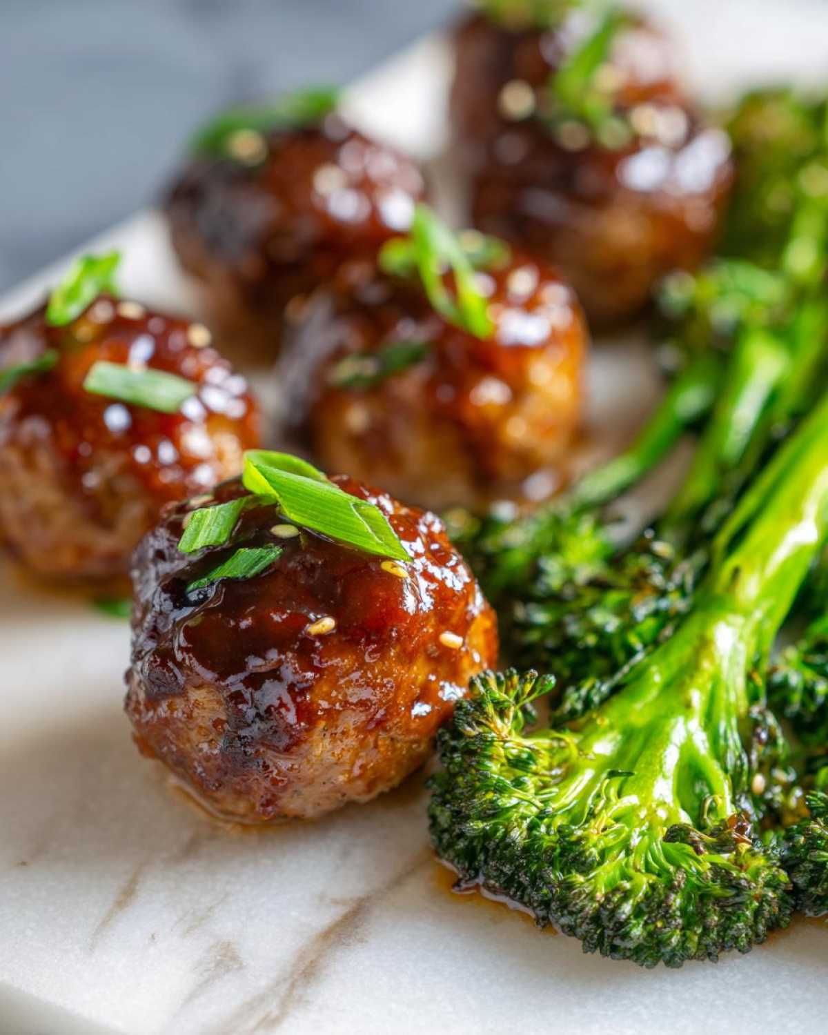 Close-up of glazed Sheet Pan Ginger Sesame Chicken Meatballs with roasted broccoli florets.