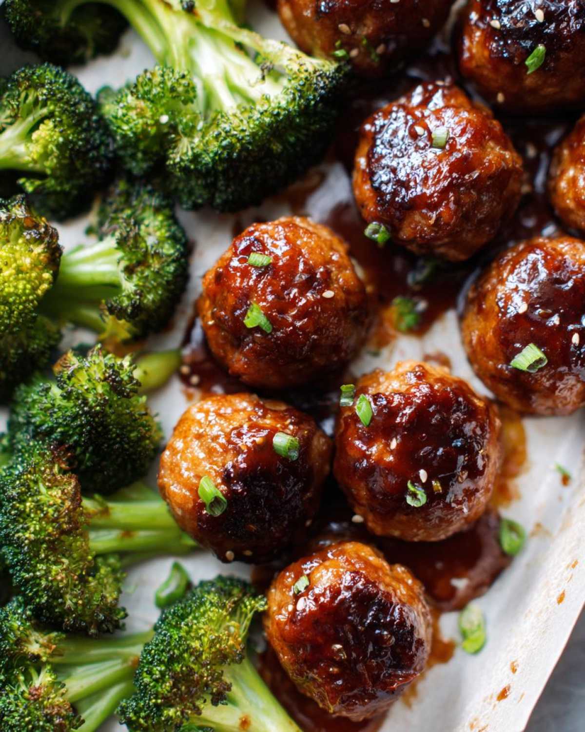 Close-up of glazed Sheet Pan Ginger Sesame Chicken Meatballs with roasted broccoli florets.