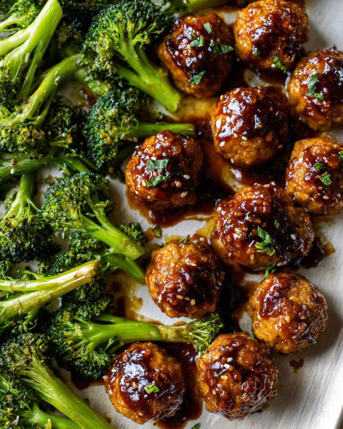 Close-up of glossy Sheet Pan Ginger Sesame Chicken Meatballs with roasted broccoli florets.