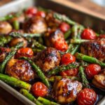 Close-up of glossy, glazed Sheet Pan Honey Balsamic Chicken with asparagus spears and roasted cherry tomatoes.