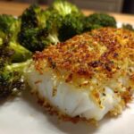 Close-up of a flaky white fish fillet with a golden Sheet Pan Parmesan Crusted Cod topping, served next to roasted broccoli.