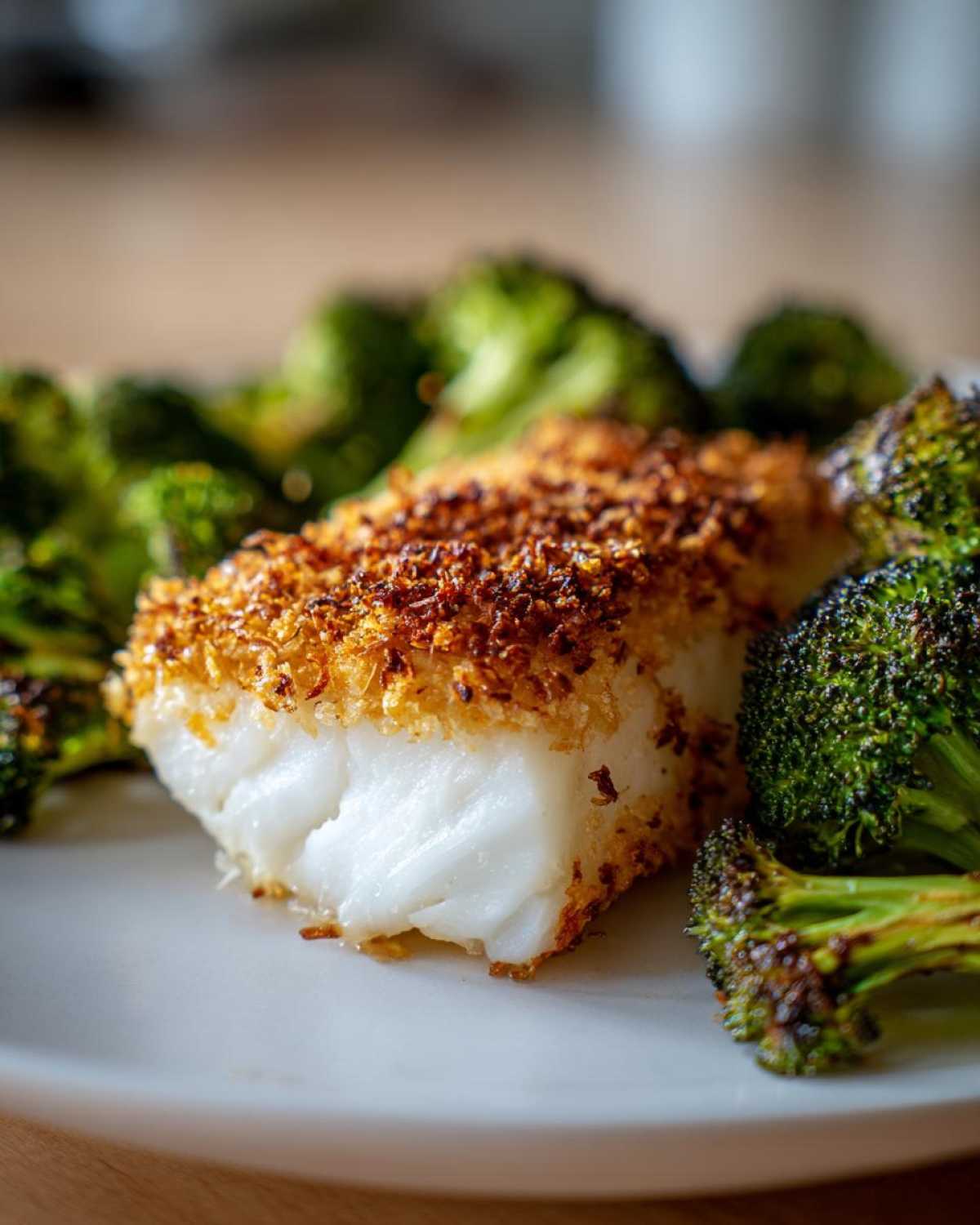 Close-up of flaky white cod topped with a golden Parmesan crust next to roasted broccoli.