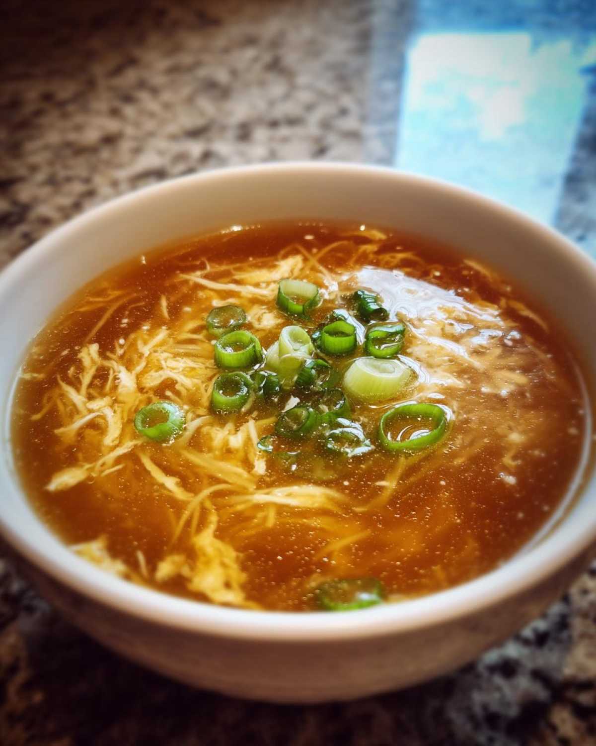 Close-up of a bowl of silky egg drop soup garnished with fresh green onions.