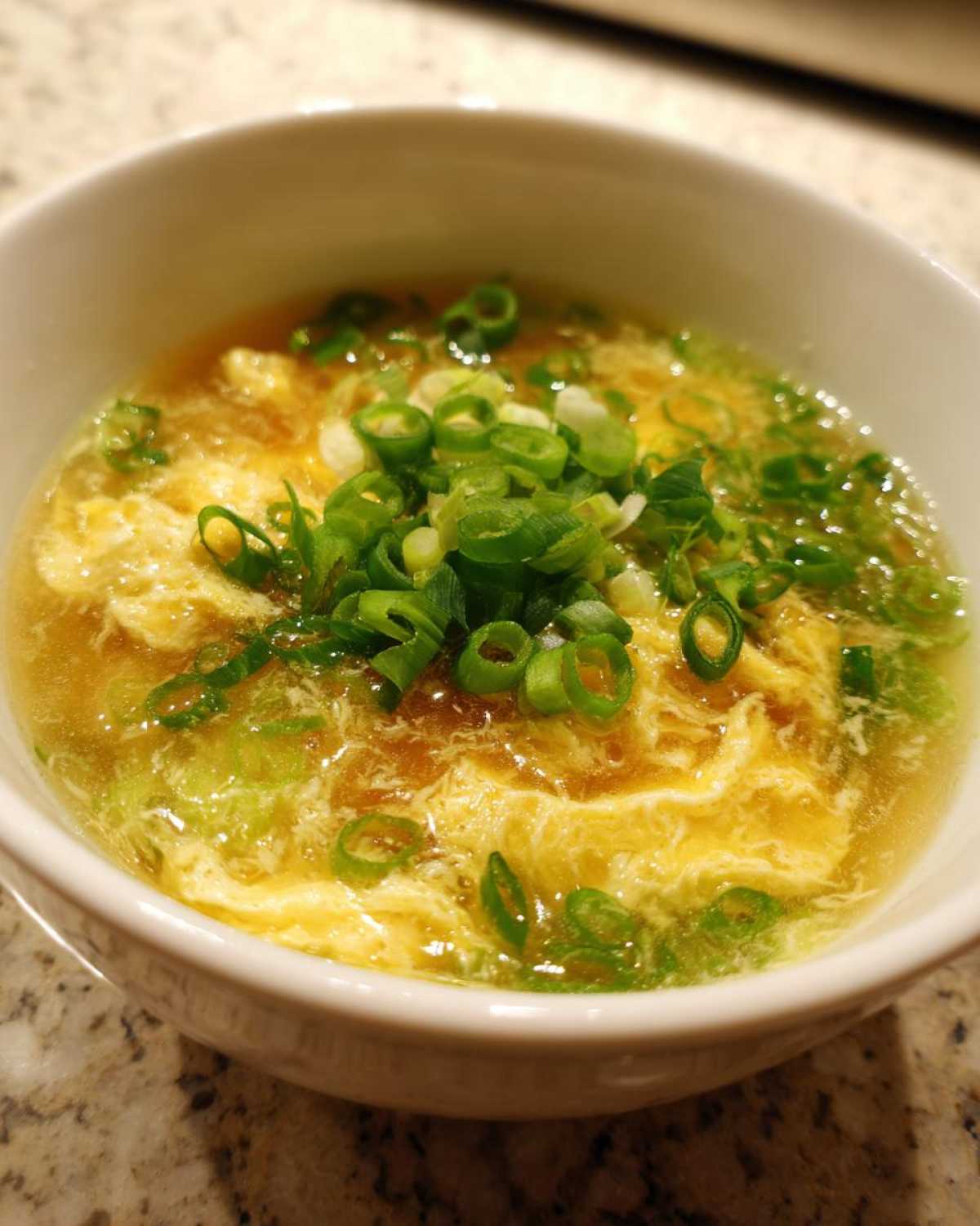 Close-up of silky egg drop soup with wispy cooked egg ribbons garnished generously with fresh sliced green onions.