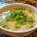 Close-up of a bowl of silky egg drop soup garnished generously with fresh green onions.